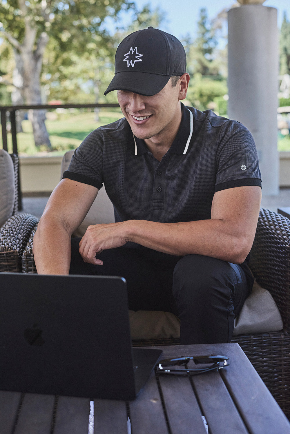 Man inMentfore Icon Hat and polo shirt using a laptop outdoors