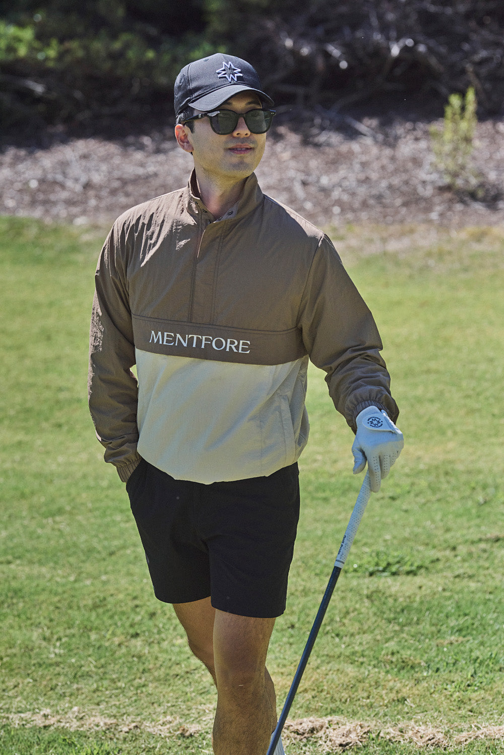 Man walking on a golf course wearing a jacket with 'Mentfore' branding.