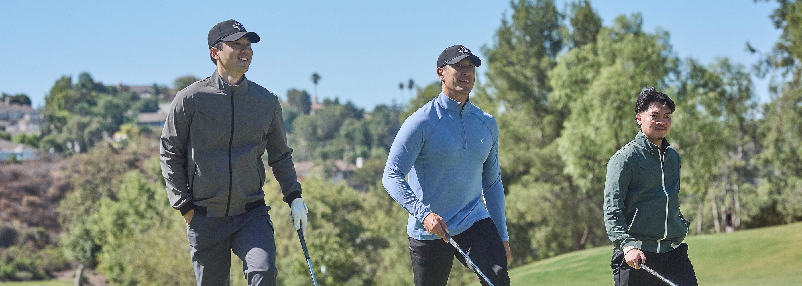 Three men playing golf on a sunny day with trees and houses in the background.
