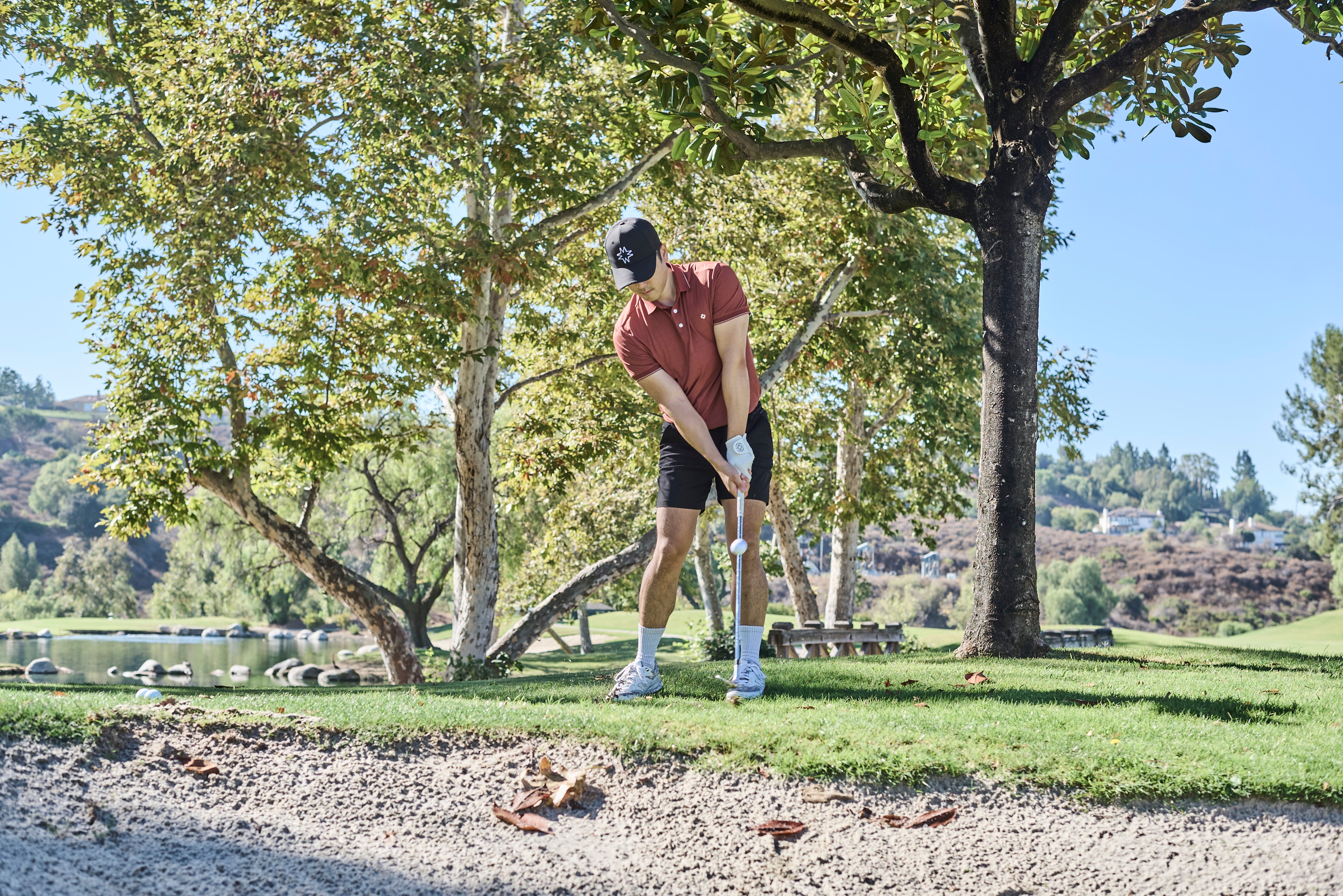 Person chipping, playing golf on a course with trees and water in the background