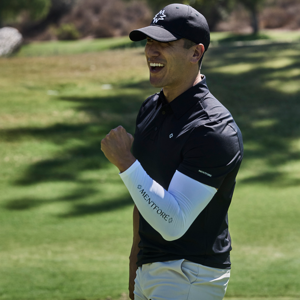 Golfer celebrating on a golf course wearing a black Mentfore Golf Polo and white Mentfore pants.